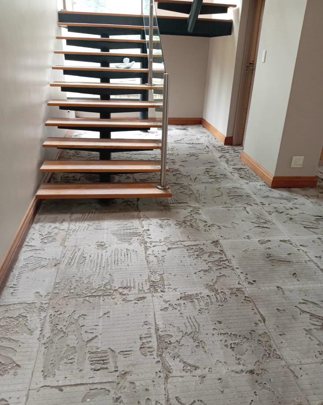 Floor tile installation in progress beneath a timber staircase